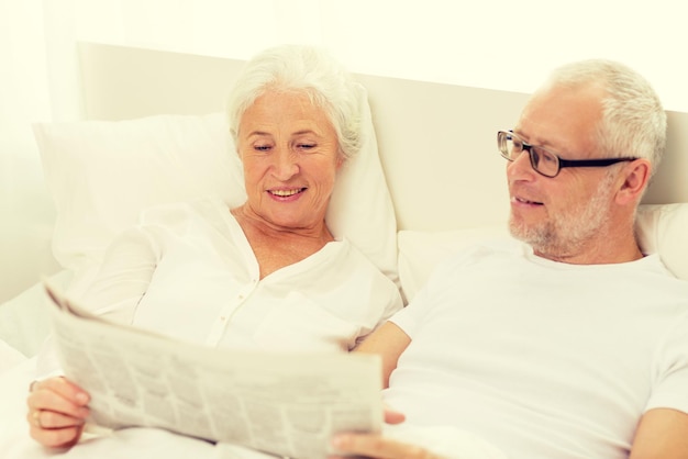 concepto de familia, hora de acostarse, descanso, edad y personas - feliz pareja senior con periódico tirado en casa