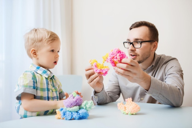 concepto de familia, infancia, creatividad, actividad y personas - padre feliz e hijo pequeño jugando con arcilla de bola en casa