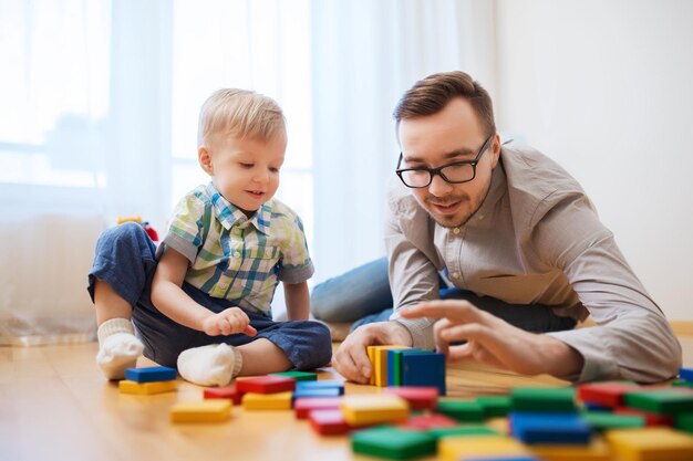 concepto de familia, infancia, creatividad, actividad y personas - padre feliz e hijo pequeño jugando con bloques de juguete en casa