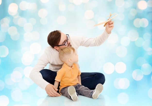 concepto de familia, infancia, paternidad, ocio y personas - padre feliz e hijo pequeño jugando con un avión de juguete sobre el fondo azul de las luces navideñas