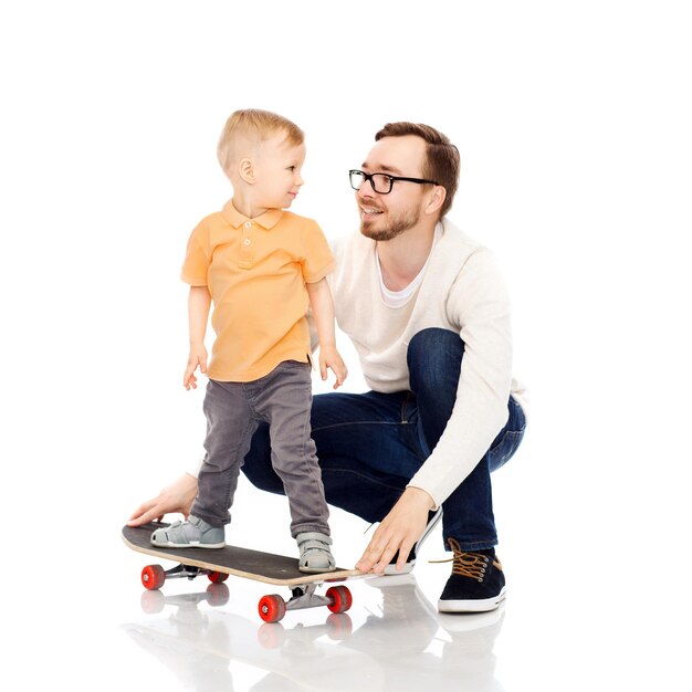 concepto de familia, infancia, paternidad, ocio y personas - padre feliz enseñando a un hijo pequeño a andar en patineta