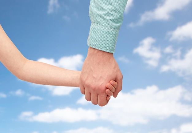 concepto de familia, infancia, paternidad y personas - padre e hijo tomándose de la mano sobre el cielo azul y el fondo de las nubes