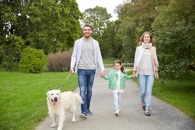 concepto de familia, mascotas, animales domésticos y personas - familia feliz con perro labrador retriever caminando en el parque de verano