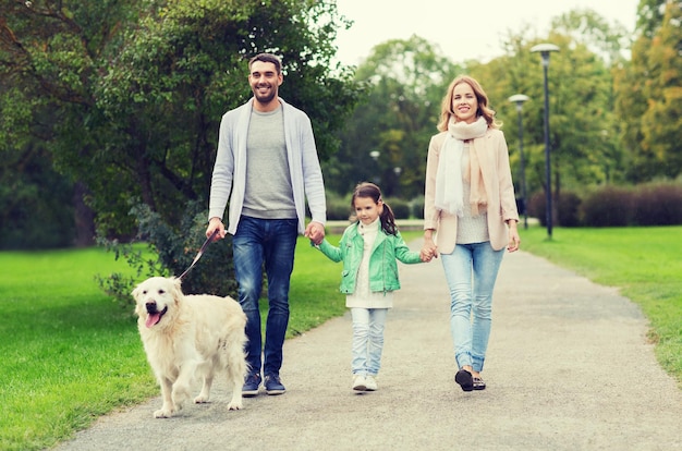 concepto de familia, mascotas, animales domésticos y personas - familia feliz con perro Labrador Retriever caminando en el parque de verano