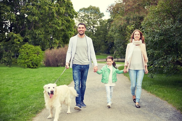 concepto de familia, mascotas, animales domésticos y personas - familia feliz con perro labrador retriever caminando en el parque de verano