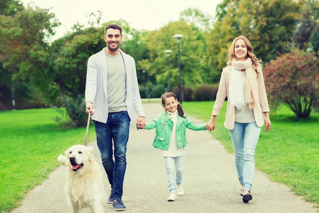 concepto de familia, mascotas, animales domésticos y personas - familia feliz con perro labrador retriever caminando en el parque de verano