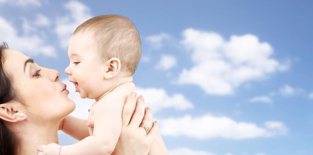 concepto de familia, maternidad, paternidad, personas y cuidado de niños - madre feliz besando a un bebé adorable sobre el fondo del cielo azul