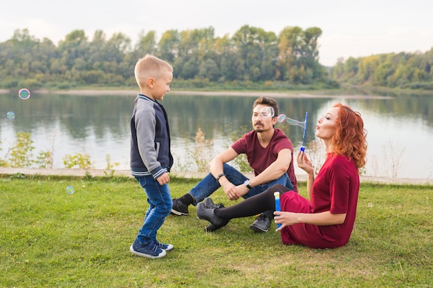 Concepto de familia y naturaleza: madre, padre y su hijo jugando con coloridas pompas de jabón