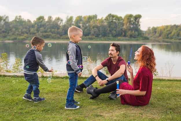 Concepto de familia y naturaleza: madre, padre y sus hijos jugando con coloridas pompas de jabón