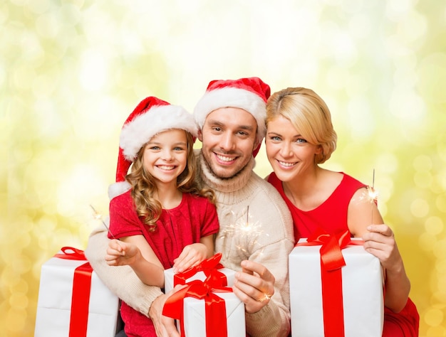 concepto de familia, navidad, navidad, felicidad y personas - familia sonriente con sombreros de ayudante de santa con muchas cajas de regalo y luces de bengala