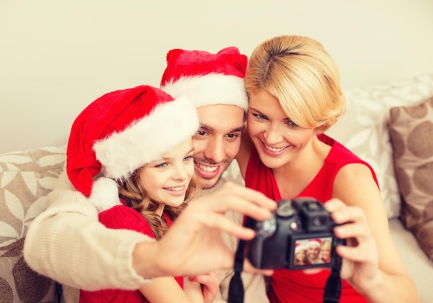 concepto de familia, navidad, navidad, felicidad y personas - familia sonriente con sombreros de ayudante de santa tomando fotos con cámara fotográfica