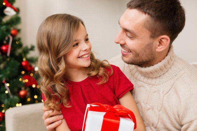 concepto de familia, navidad, navidad, felicidad y personas - padre e hija sonrientes sosteniendo una caja de regalo y mirándose el uno al otro