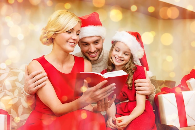 concepto de familia, Navidad, Navidad, invierno, felicidad y personas - familia sonriente con sombreros de ayudante de santa con muchas cajas de regalo, libro de lectura