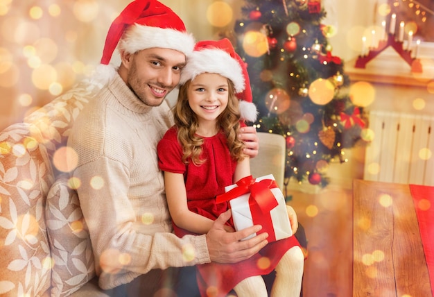 concepto de familia, navidad, navidad, invierno, felicidad y personas - padre e hija sonrientes en sombreros de ayudante de santa con caja de regalo