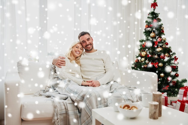 concepto de familia, Navidad, vacaciones, amor y personas - pareja feliz cubierta de cuadros sentados en el sofá en casa