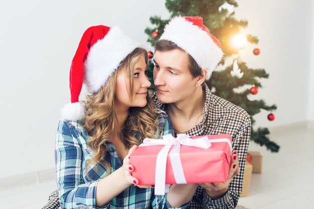 Concepto de familia, Navidad, vacaciones de invierno y personas - feliz pareja abrazándose cerca del árbol de Navidad en casa.