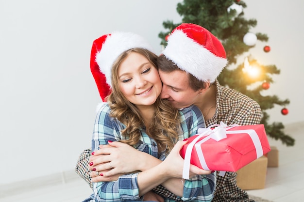 Concepto de familia, Navidad, vacaciones de invierno y personas - feliz pareja abrazándose cerca del árbol de Navidad en casa.