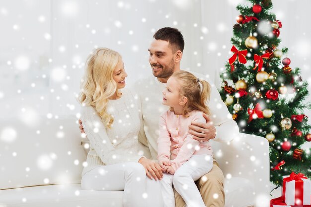 concepto de familia, navidad, vacaciones y personas - feliz madre, padre e hija pequeña sentada en el sofá en casa