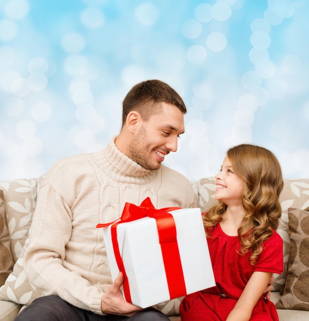 concepto de familia, navidad, vacaciones y personas: padre e hija sonrientes con caja de regalo sobre fondo de luces azules