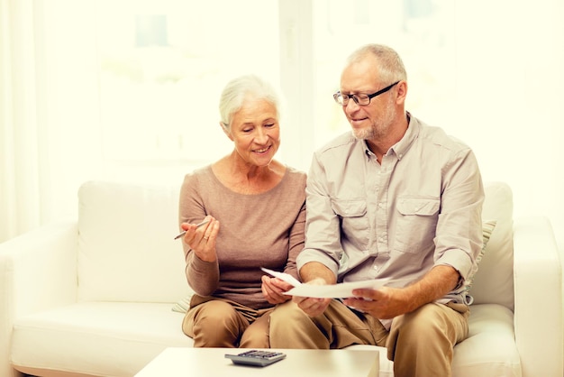 concepto de familia, negocios, ahorros, edad y personas - pareja senior sonriente con papeles y calculadora en casa