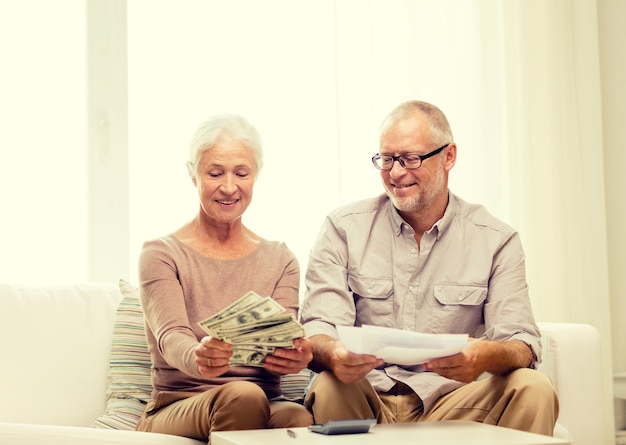 Foto concepto de familia, negocios, ahorros, edad y personas - pareja senior sonriente con papeles, dinero y calculadora en casa