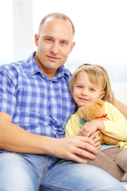 concepto de familia, niño y felicidad - padre e hija sonrientes con oso de peluche en casa