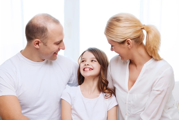 concepto de familia, niño y hogar - padres sonrientes y niña en casa