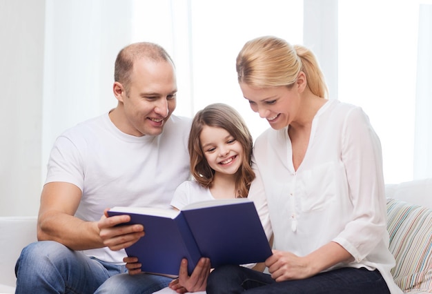 concepto de familia, niño y hogar - padres sonrientes y niñita con libro en casa