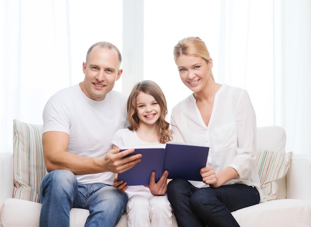 concepto de familia, niño y hogar - padres sonrientes y niñita con libro en casa