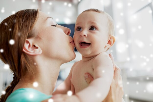 concepto de familia, niño y paternidad - primer plano de una madre feliz y sonriente besando a su bebé en casa sobre la nieve