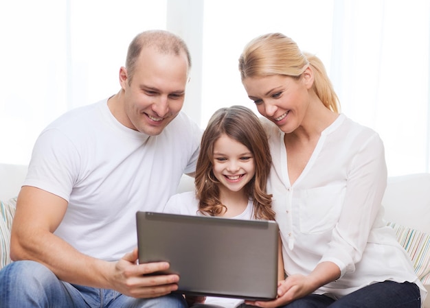 concepto de familia, niño, tecnología y hogar - padres sonrientes y niñita con laptop en casa