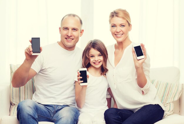 concepto de familia, niño, tecnología y hogar - padres sonrientes y niñita con smartphones de pantalla negra en blanco en casa