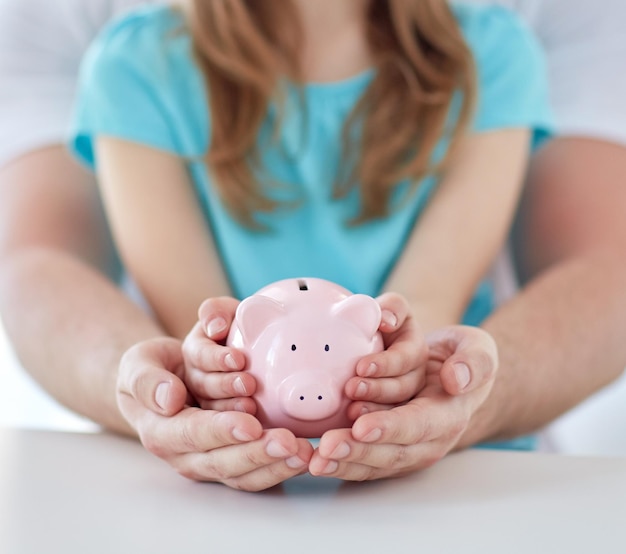 concepto de familia, niños, dinero, inversiones y personas - cierre de las manos de padre e hija sosteniendo una alcancía rosa