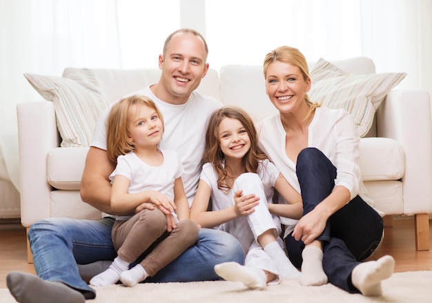 concepto de familia, niños y hogar - familia sonriente con dos niñas pequeñas sentadas en el suelo en casa