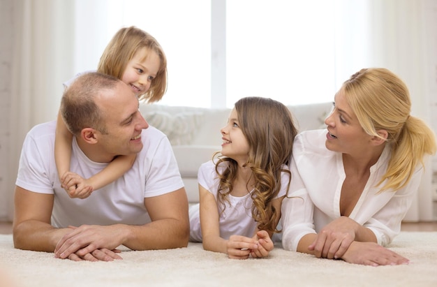 concepto de familia, niños y hogar - familia sonriente con dos niñas pequeñas tiradas en el suelo en casa