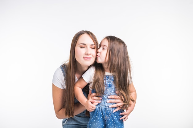 Concepto de familia, niños y paternidad - mujer joven con su pequeño niño lindo en la pared blanca. Mamá con hija aislada.