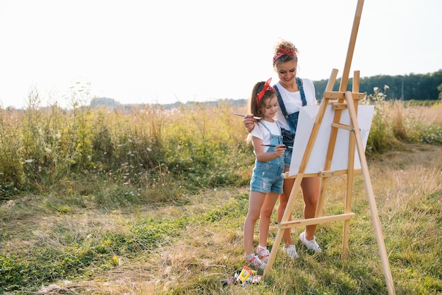 Concepto de familia, niños y personas - feliz madre e hija dibujando y hablando sobre una superficie verde