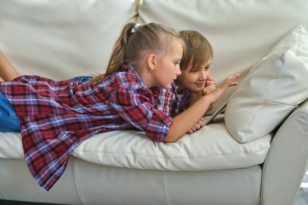 Concepto de familia, niños, tecnología y hogar: hermano y hermana sonrientes con tablet pc en el sofá de la sala de estar