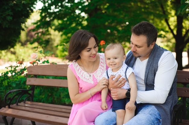 Concepto de la familia, de la paternidad, de la adopción y de la gente - madre feliz, padre y niño pequeño que caminan en parque del verano.