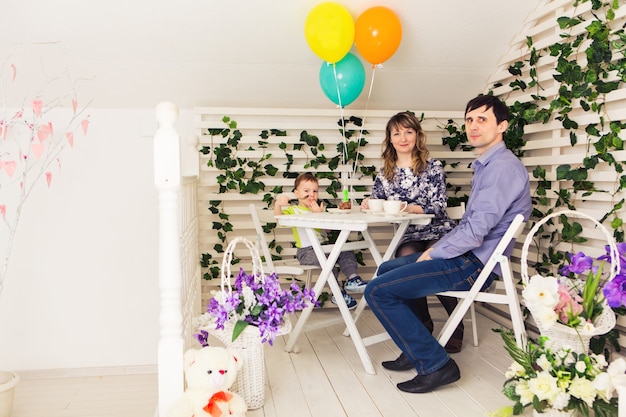 Concepto de familia, paternidad, feliz cumpleaños y vacaciones: padres felices y un niño en una mesa bebiendo té y comiendo pastel.