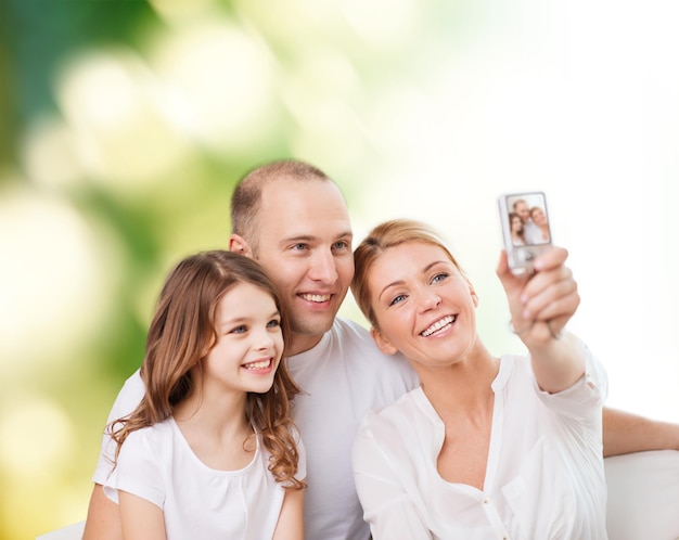 concepto de familia, tecnología, ecología y personas - madre sonriente, padre y niña haciendo selfie con cámara sobre fondo verde