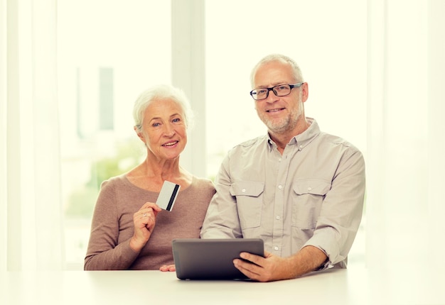 concepto de familia, tecnología, edad y personas - feliz pareja de ancianos con tablet pc y tarjeta de crédito en casa