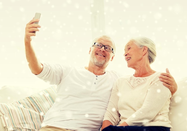 concepto de familia, tecnología, edad y personas - feliz pareja mayor con smartphone tomando selfie en casa