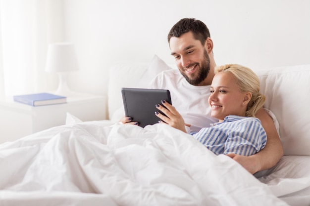 concepto de familia, tecnología, internet y personas: pareja feliz sonriente con computadora tablet pc en la cama en el dormitorio de casa