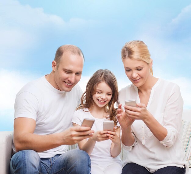 concepto de familia, tecnología y personas: madre, padre y niña sonrientes con smartphones sobre fondo de cielo azul