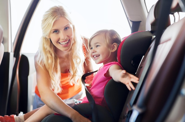 Foto concepto de familia, transporte, seguridad, viaje por carretera y personas - madre feliz sujetando al niño con el cinturón de seguridad del coche