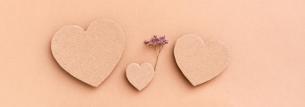 Concepto de familia. Tres corazones de cartón: un niño con una flor seca entre padres sobre un fondo beige. Vista superior. Banner web