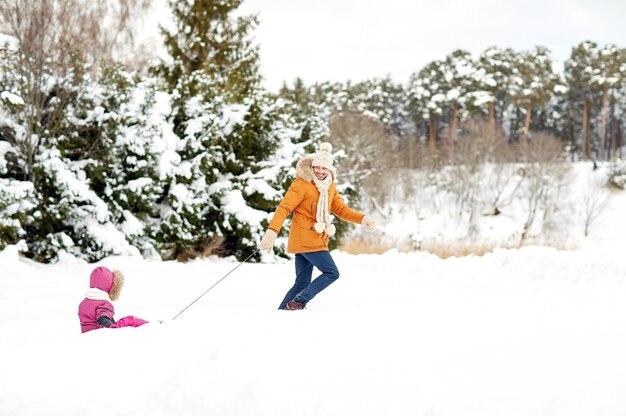 concepto de familia, trineo, temporada y gente - padre feliz tirando del trineo con el niño al aire libre en invierno