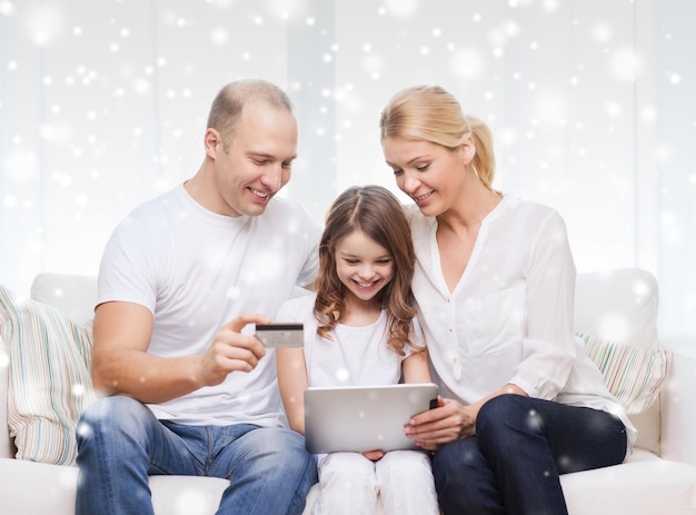 concepto de familia, vacaciones, compras, tecnología y personas - familia feliz con tablet pc y tarjeta de crédito sobre fondo de copos de nieve