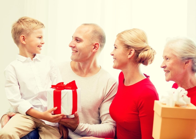 concepto de familia, vacaciones, generación, navidad y personas - familia sonriente con cajas de regalo sentadas en el sofá en casa
